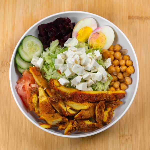 A colorful salad bowl with chicken, lettuce, feta, chickpeas, beets, cucumber, tomato, and hard-boiled eggs.