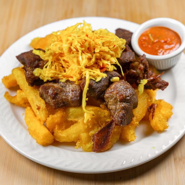 A white plate holds a dish of fried plantains, stewed meat, yellow cabbage, and a side of red sauce.