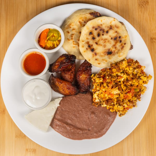 A white plate with pupusas, scrambled eggs, refried beans, fried plantains, cheese, and sauces.