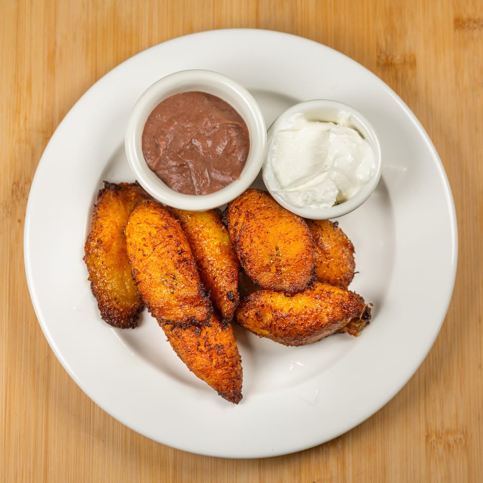 Fried plantains with two dipping sauces, one brown and one white, on a white plate.