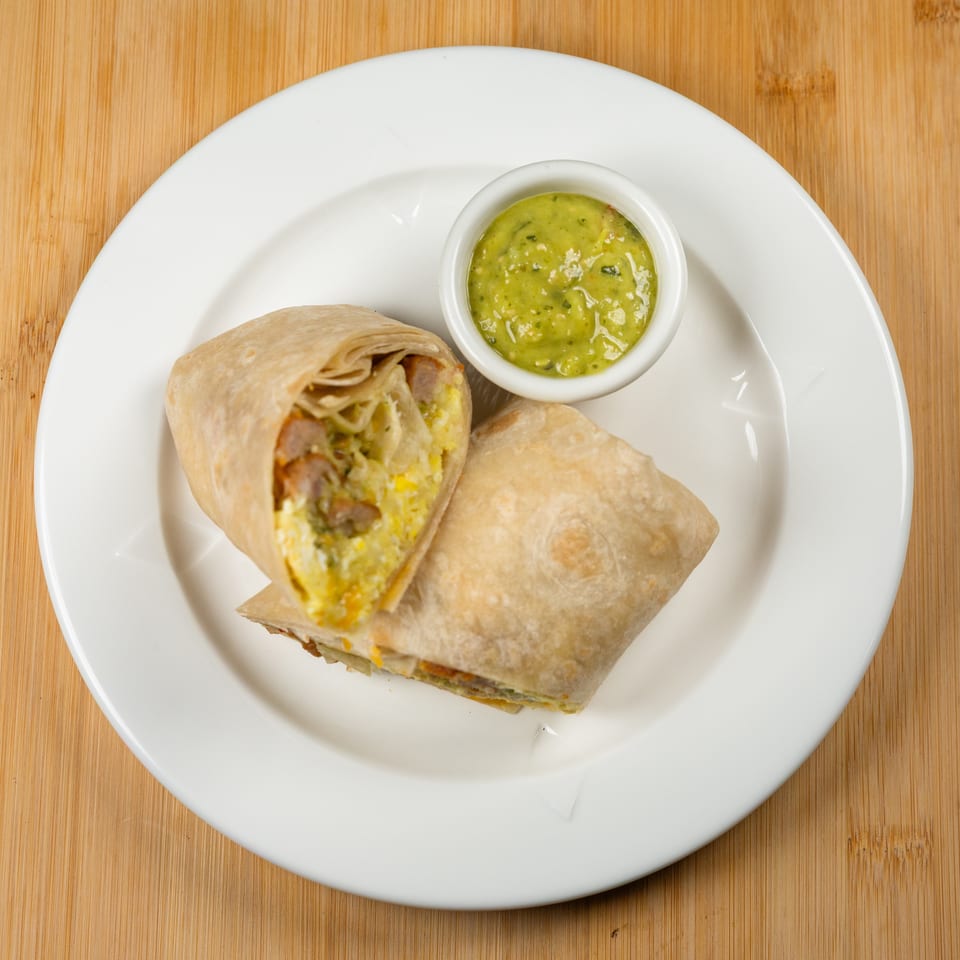 Breakfast burrito, cut in half, with a side of green salsa on a white plate.