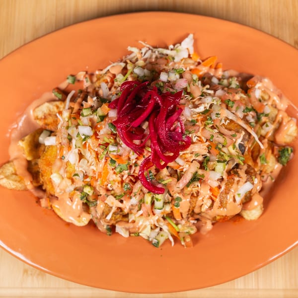 An orange plate filled with loaded fries topped with salsa, pickled red onions, and a creamy sauce.