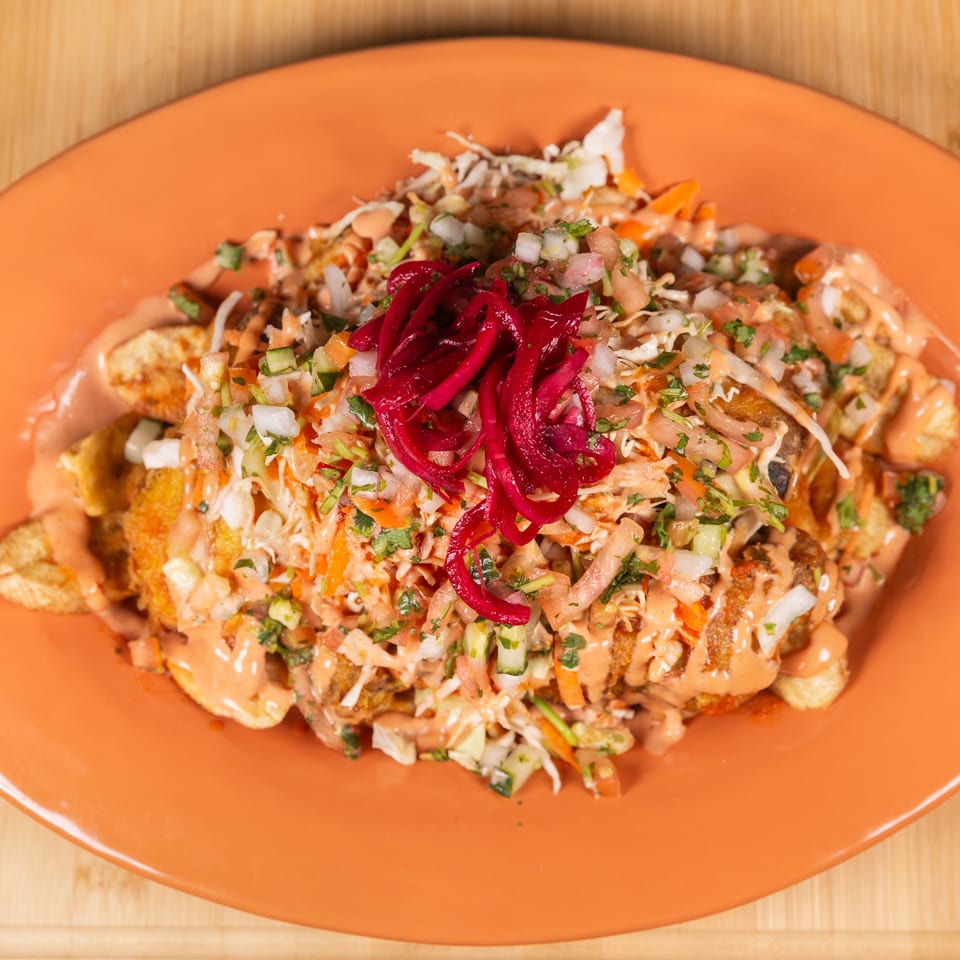 An orange plate filled with loaded fries topped with salsa, pickled red onions, and a creamy sauce.
