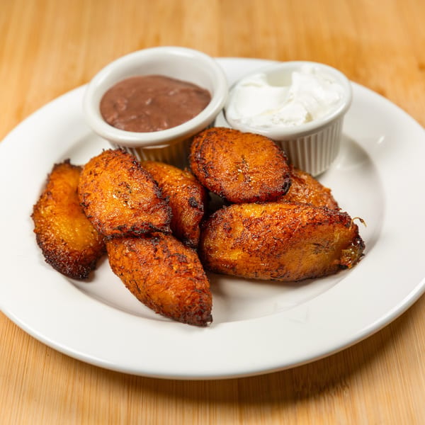Fried plantains with two dipping sauces, one brown and one white, on a white plate.