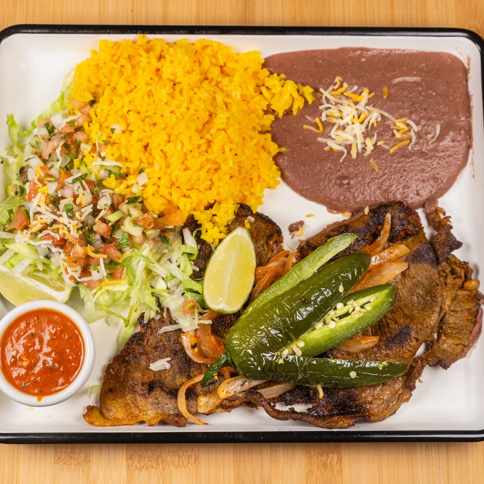 Grilled steak with rice, refried beans, salad, salsa, lime, and jalapeños on a white plate.
